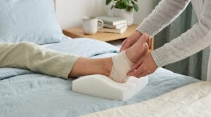 Une personne ajuste un bandage sur le talon d'un patient reposant sur un coussin en mousse dans un lit.